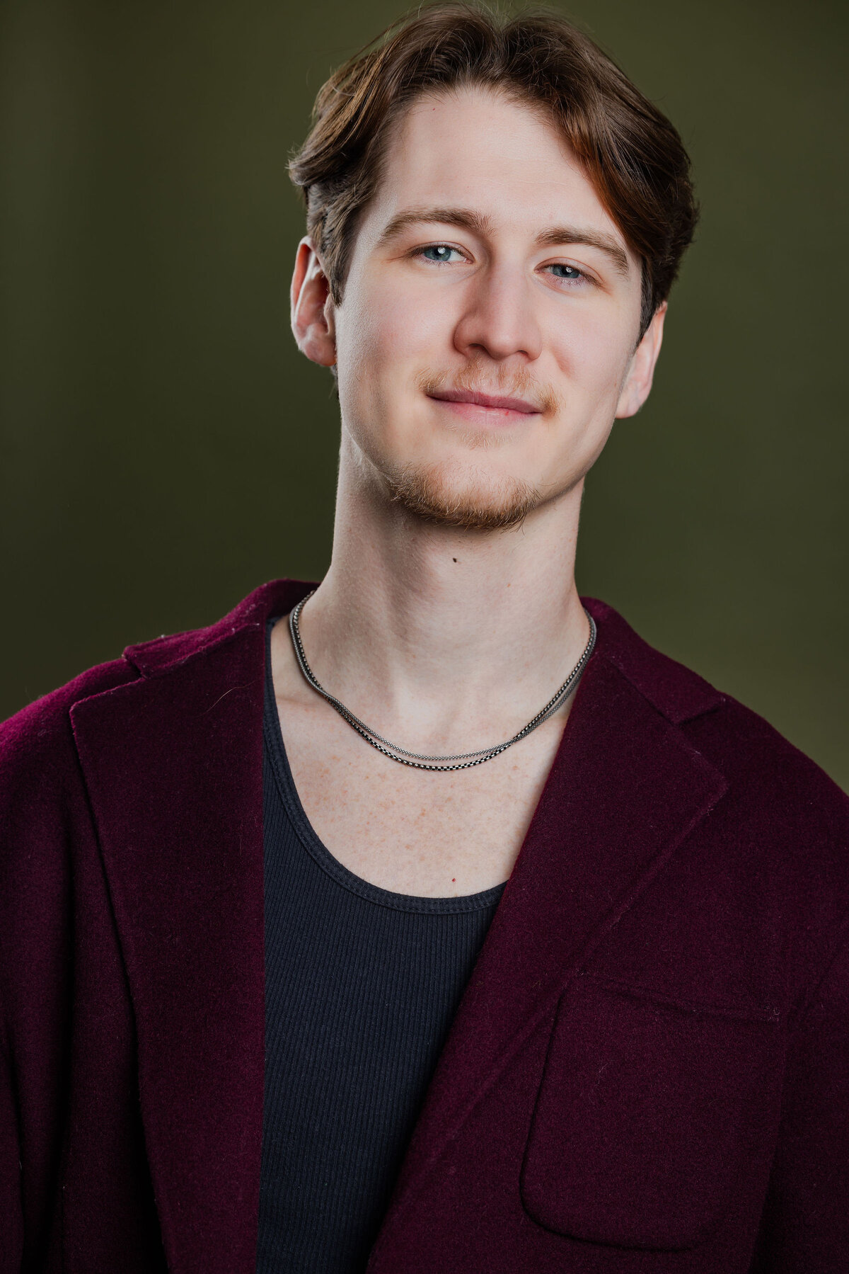 Anthony Edward, headshot — burgundy cardigan on green background